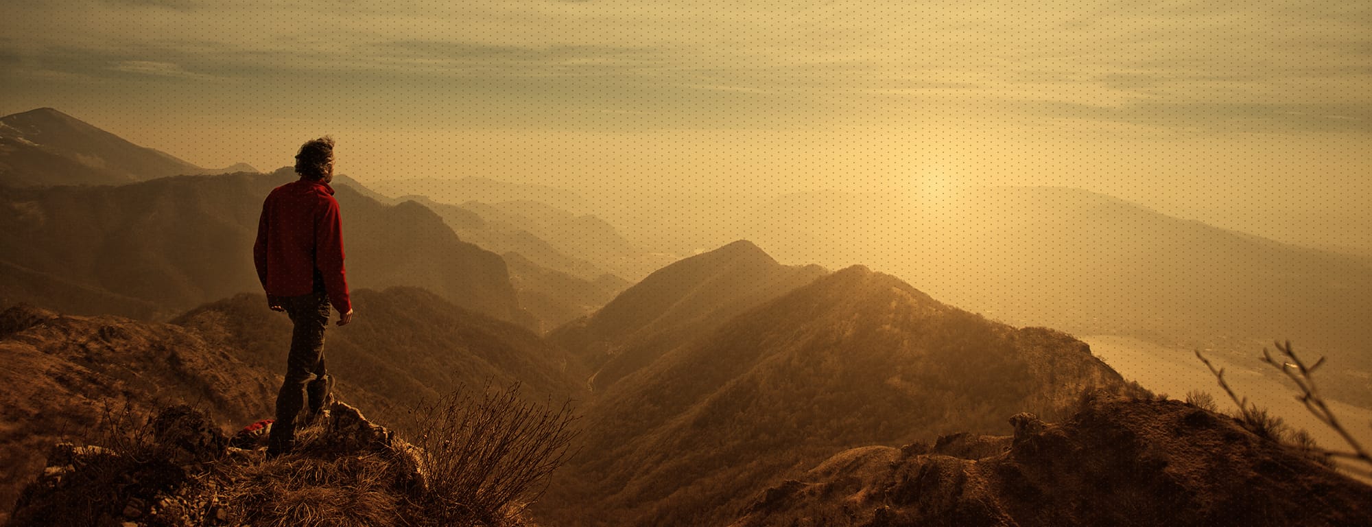 Man in red jacket, atop a mountain look across the horizon