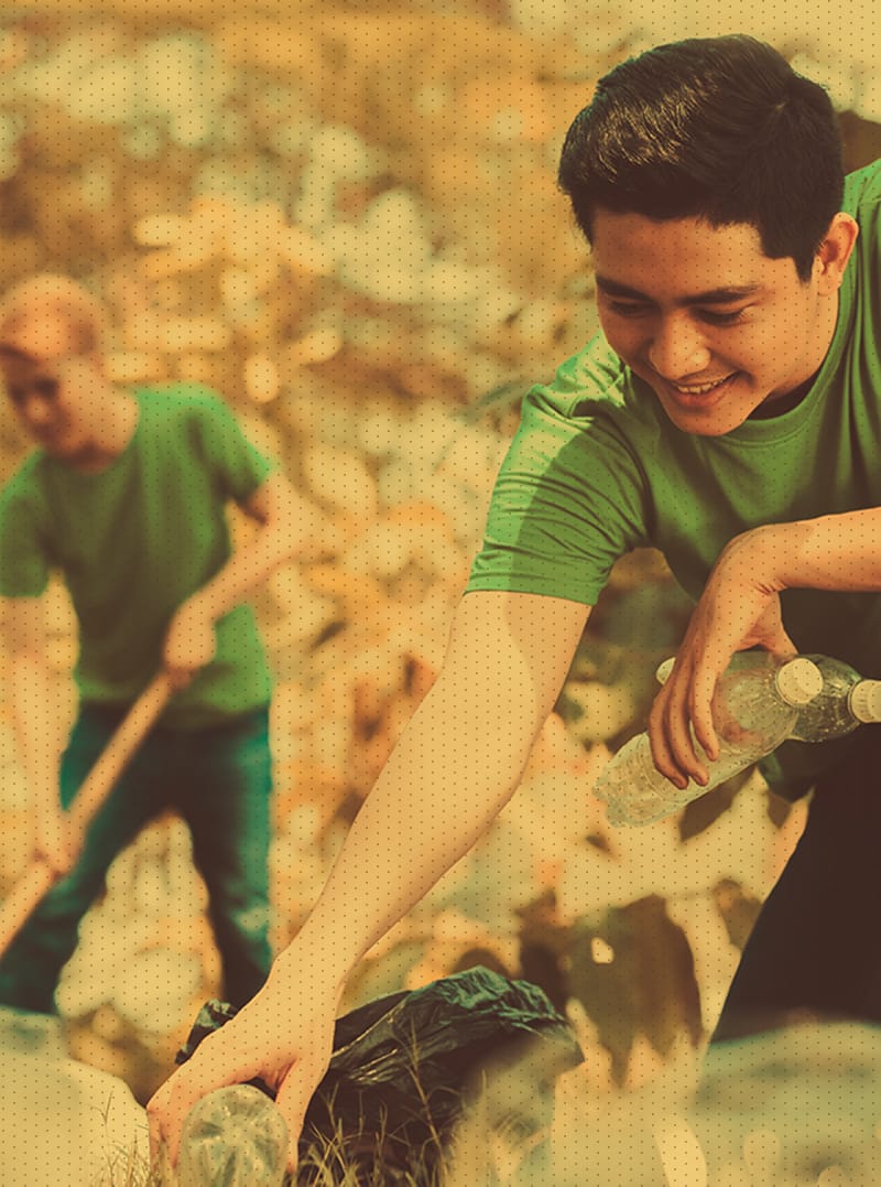 Male, kneeling, picking up trash and recycling in park and disposing of it properly