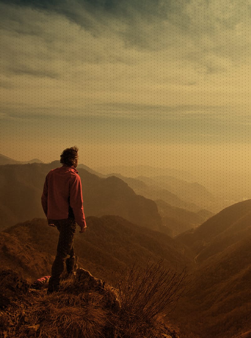Man in red jacket, atop a mountain look across the horizon
