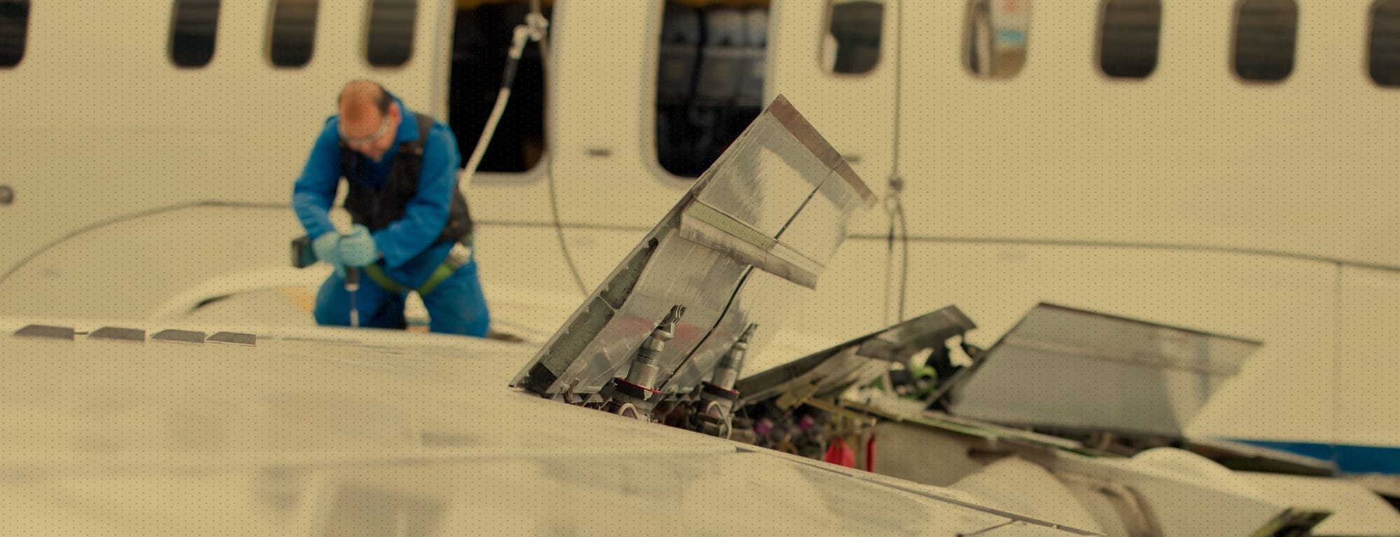 Man in blue, working a top of plane wing performing maintenance