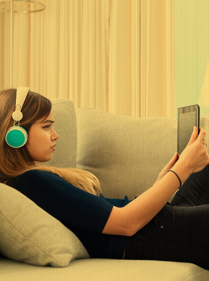 Women on couch wearing headphones looking at tablet