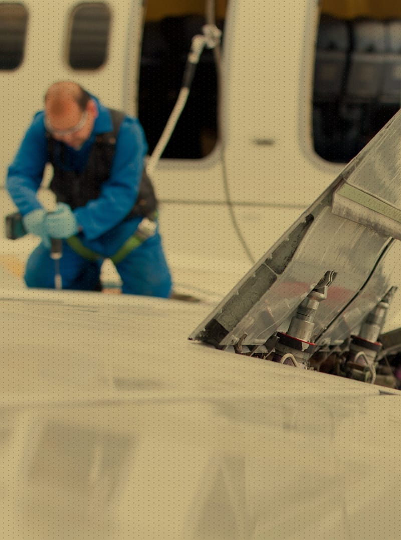 Man in blue, working a top of plane wing performing maintenance