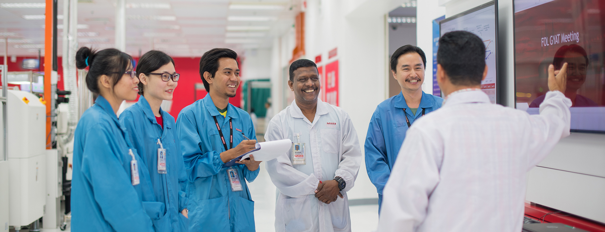 group of diverse women and men in lab coats talking and looking at a screen