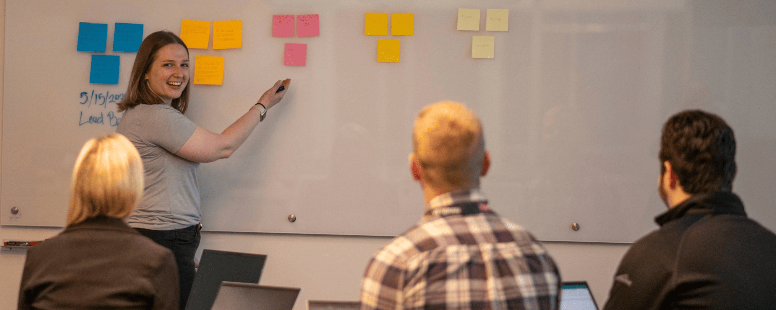 a person writing on and pointed at a whiteboard covered in sticky notes