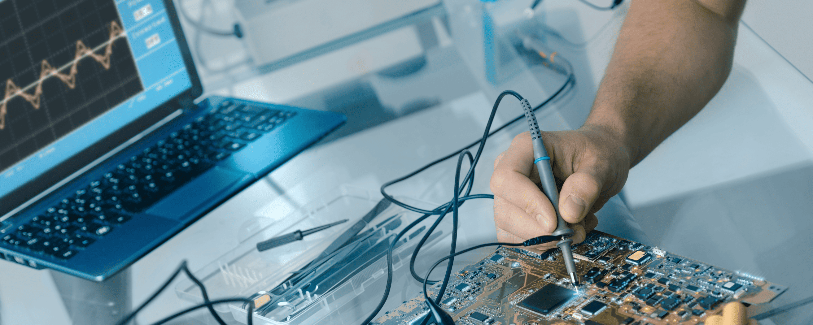close-up of a hand using test equimpment on a circuit board connected to a computer