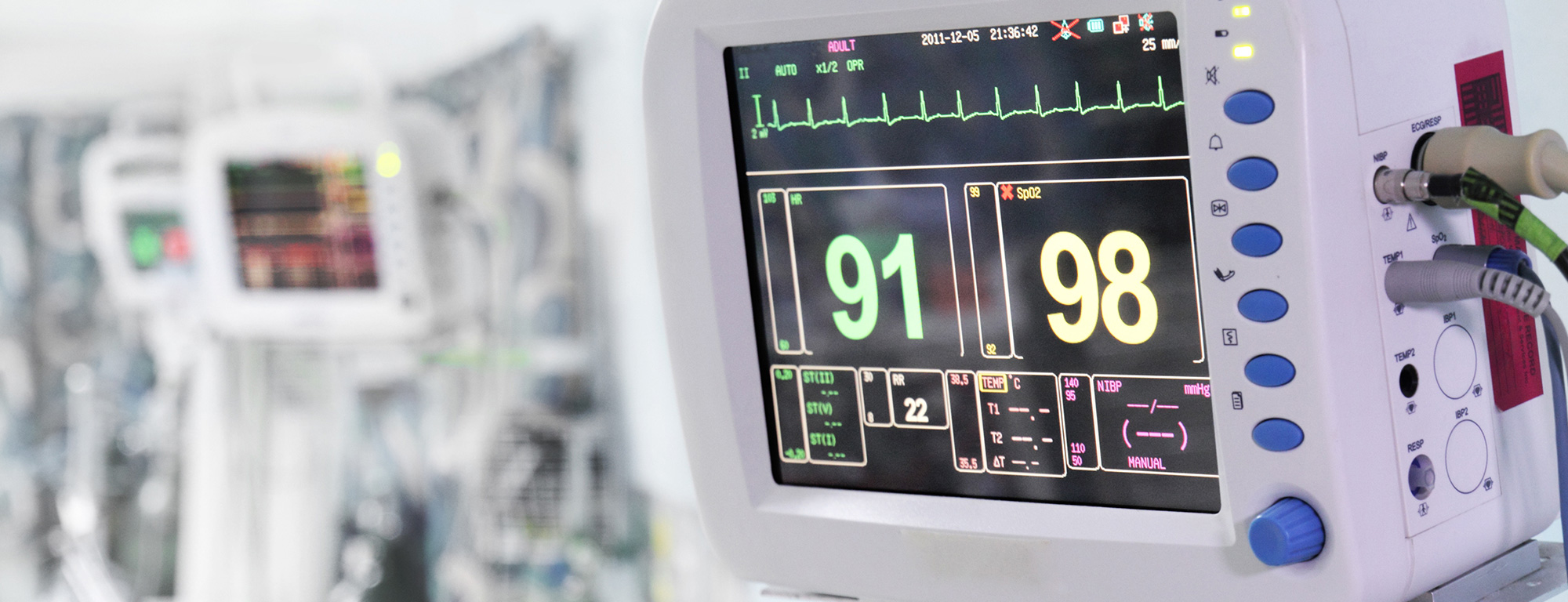 A close-up of a hospital vital signs monitor displaying heart rate, oxygen saturation, and other patient health metrics in a clinical setting.