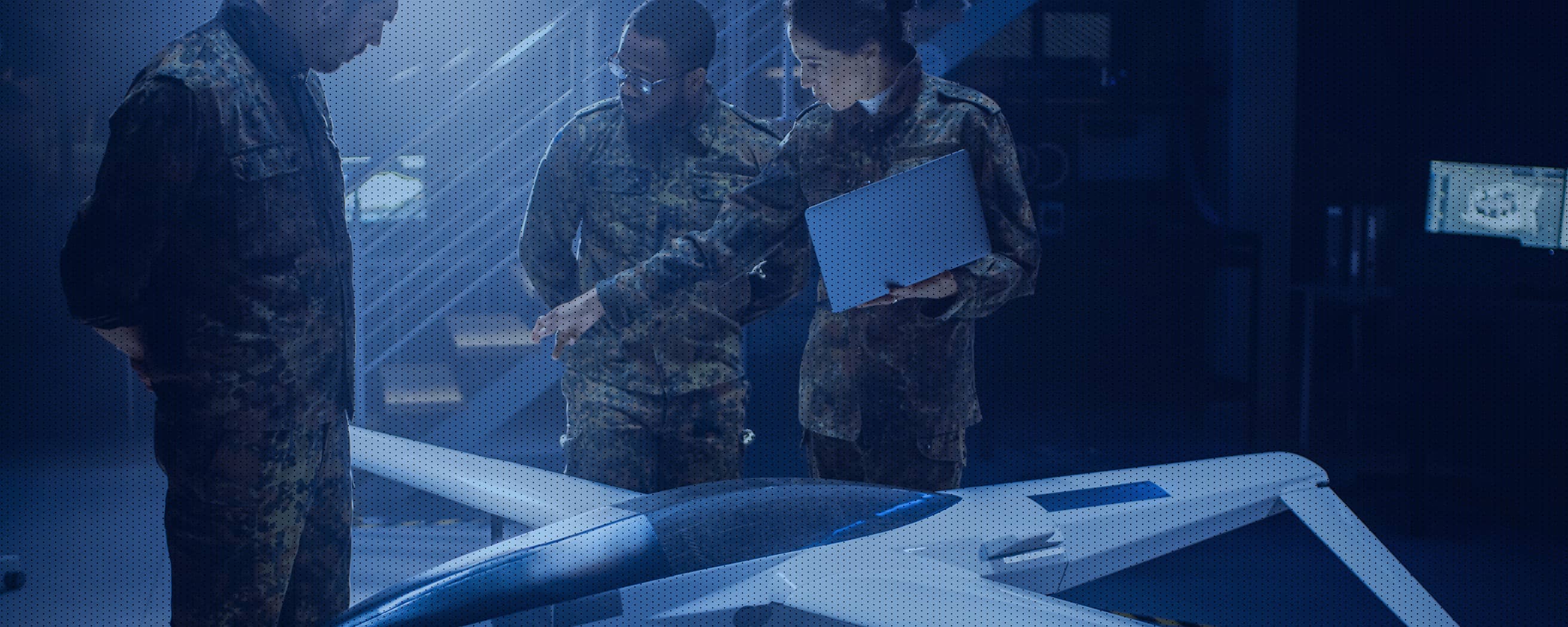 Military personnel examine a high-tech unmanned aerial vehicle (UAV) prototype in a dimly lit research facility.