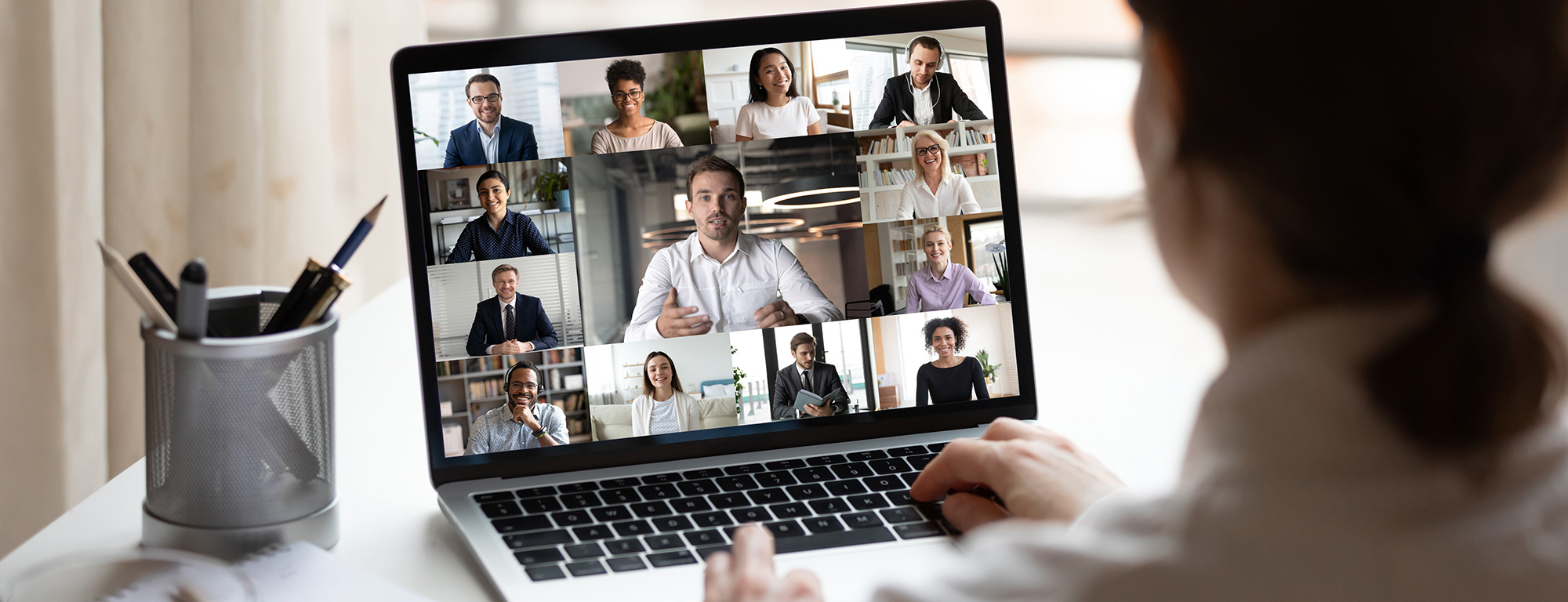 A person participates in a virtual video conference on a laptop, viewing a grid of diverse colleagues in an online meeting.