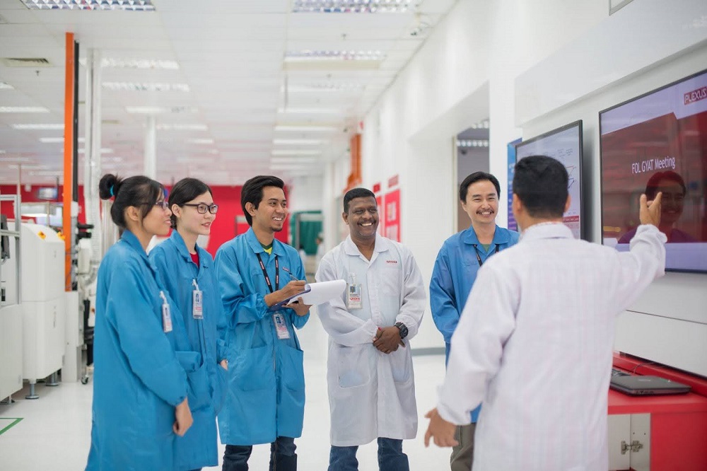 Plexus employees engaging in a stand-up meeting on the manufacturing floor, fostering internal awareness and collaboration.